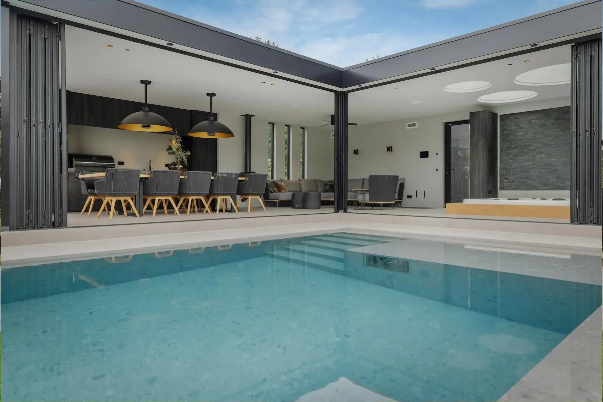 Impressie van een deel van een infinity edge pool, gelegen naast een modern poolhouse. Het landschapszwembad heeft natuursteenlook randen en een trap.