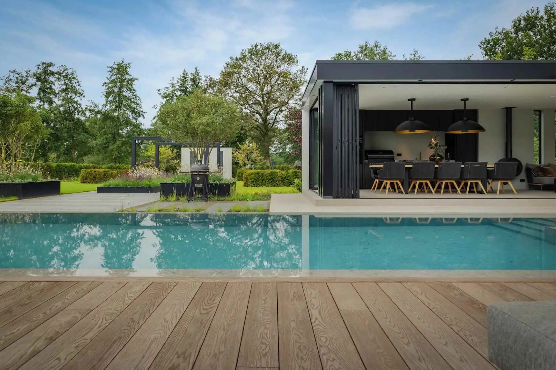 Impressie van een infinity edge pool met zonneterras, in een royale tuin met poolhouse.