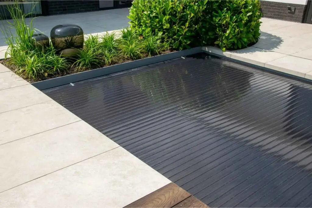 Impressie van een tuin met een plunge pool, voorzien van een zwart lamellen afdekking.