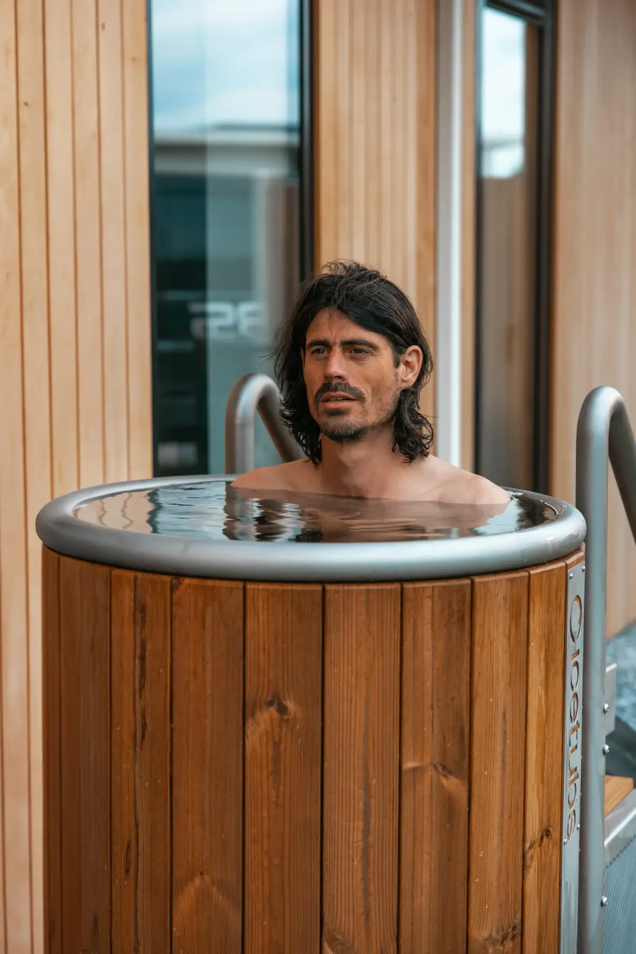 Man die een ijsbad neemt in een rond houten koudwaterbad.